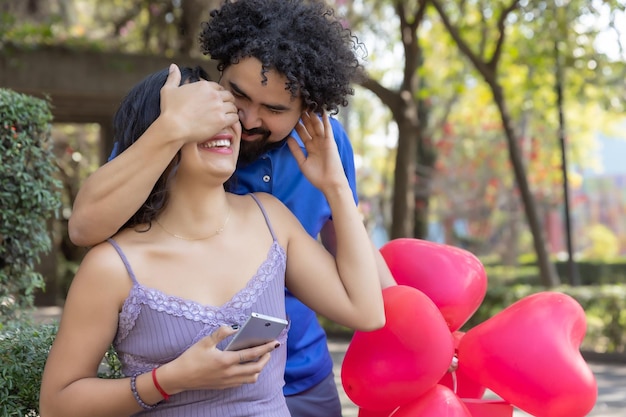 젊은 멕시코 남자는 발렌타인 데이에 그녀의 눈을 가리고 공원에서 그의 여자 친구를 놀라게
