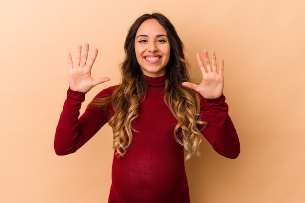 Young mexican pregnant woman isolated on beige background showing number ten with hands.