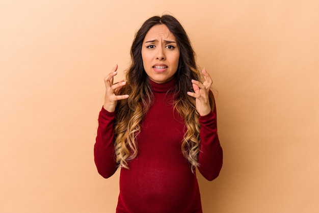 Young mexican pregnant woman isolated on beige wall upset screaming with tense hands.