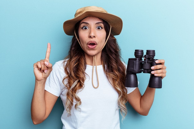 Young mexican woman holding binoculars isolated on blue background having some great idea, concept of creativity.