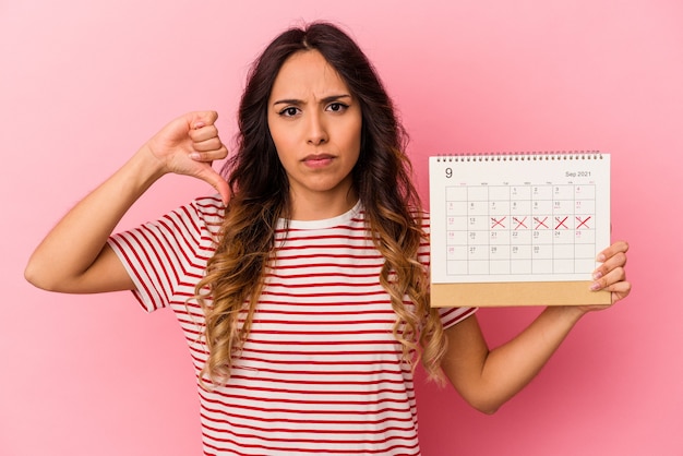 Young mexican woman holding a calendar isolated on pink background showing a dislike gesture, thumbs down. Disagreement concept.