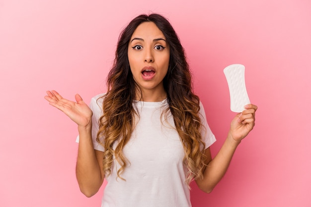 Young mexican woman holding a compress isolated on pink background surprised and shocked.