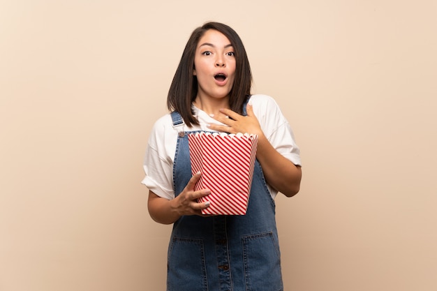 young mexican woman over isolated background holding a bowl of popcorns