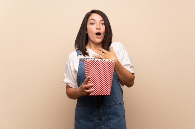 Young Mexican woman over isolated background holding a bowl of popcorns