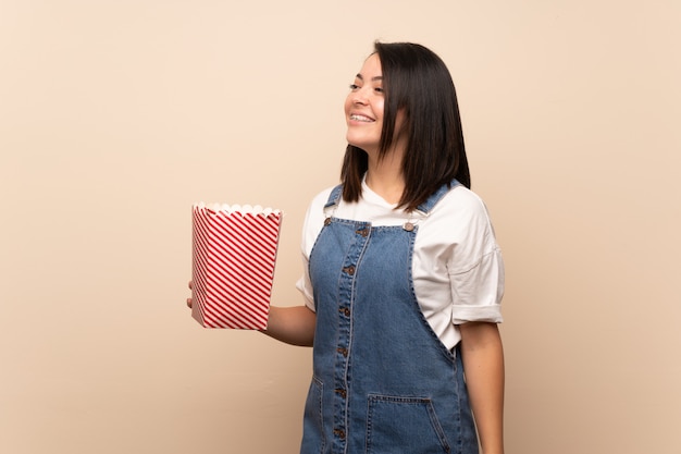 Young Mexican woman over isolated background holding a bowl of popcorns