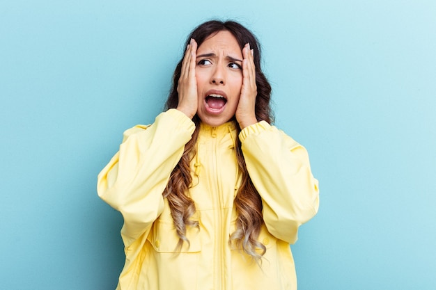 Young mexican woman isolated on blue background covering ears with hands trying not to hear too loud sound.