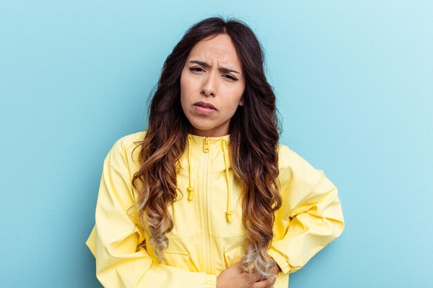 Young mexican woman isolated on blue background having a liver pain, stomach ache.