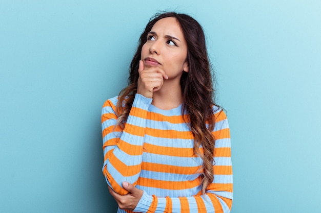 Young mexican woman isolated on blue background looking sideways with doubtful and skeptical expression.