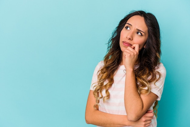 Young mexican woman isolated on blue background relaxed thinking about something looking at a copy space.