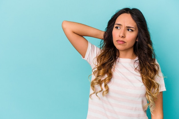 Young mexican woman isolated on blue background touching back of head, thinking and making a choice.