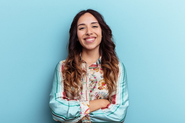 Young mexican woman isolated on blue background who feels confident, crossing arms with determination.