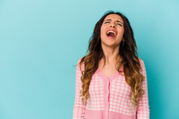 Young mexican woman isolated on blue shouting very angry, rage concept, frustrated.