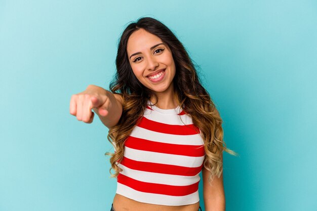 Young mexican woman isolated on blue wall cheerful smiles pointing to front.