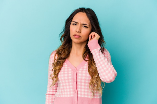 Young mexican woman isolated on blue wall covering ears with fingers, stressed and desperate by a loudly ambient.