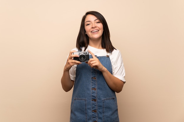 Giovane donna messicana sopra isolata che tiene una macchina fotografica