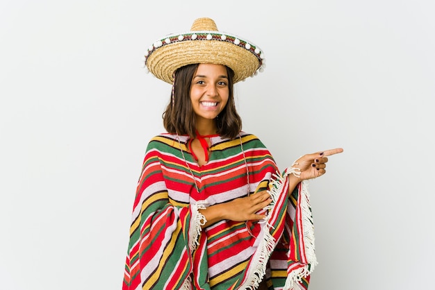 Фото Молодая мексиканская женщина изолирована на белой стене, весело улыбаясь, указывая указательным пальцем в сторону