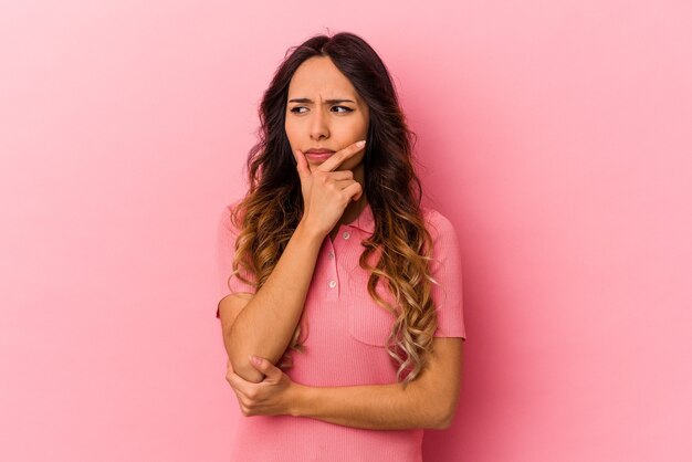 Young mexican woman isolated on pink background contemplating, planning a strategy, thinking about the way of a business.