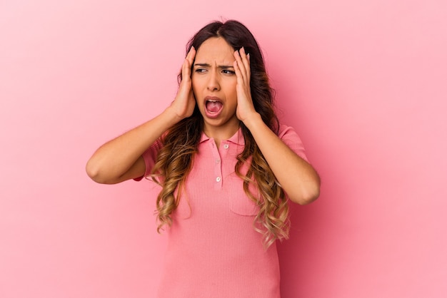 Young mexican woman isolated on pink background covering ears with hands trying not to hear too loud sound.