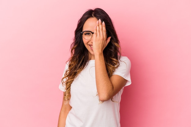 Young mexican woman isolated on pink background having fun covering half of face with palm.