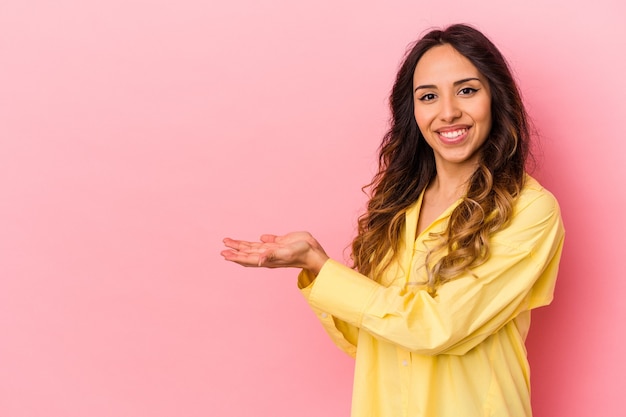 Young mexican woman isolated on pink background holding a copy space on a palm.