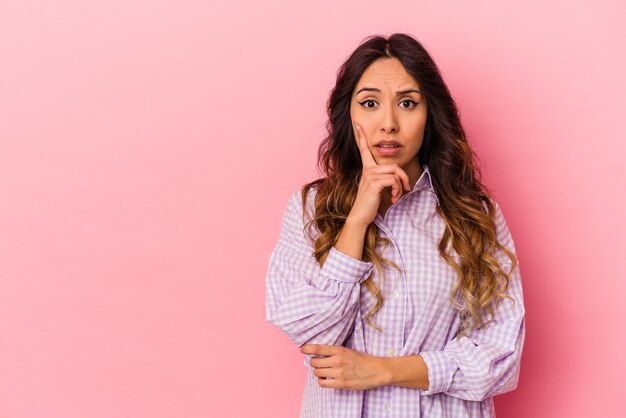 Young mexican woman isolated on pink background looking sideways with doubtful and skeptical expression.