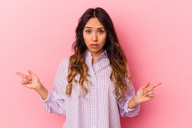 Young mexican woman isolated on pink background pointing to different copy spaces, choosing one of them, showing with finger.