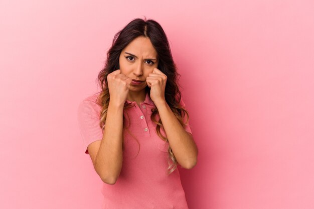 Young mexican woman isolated on pink background throwing a punch, anger, fighting due to an argument, boxing.