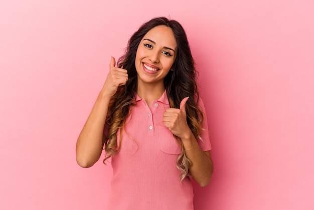 두 엄지 손가락, 미소와 자신감을 제기하는 분홍색 벽에 고립 된 젊은 멕시코 여자.