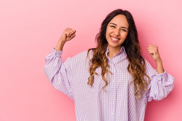 Young mexican woman isolated on pink wall raising fist after a victory, winner concept.