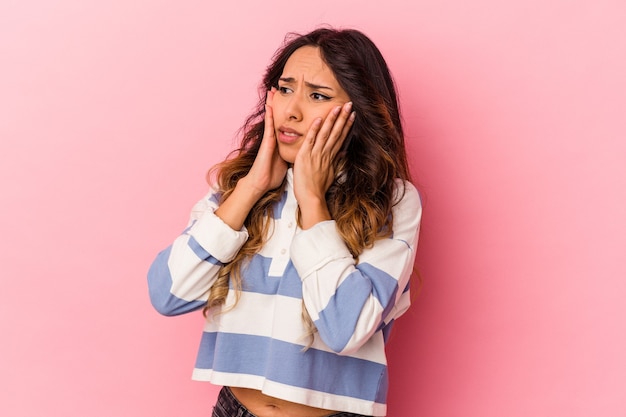 Young mexican woman isolated on pink wall scared and afraid.