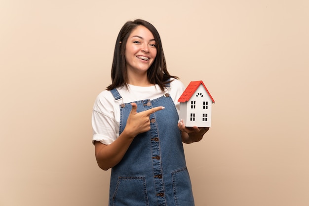 Young Mexican woman over isolated wall holding a little house