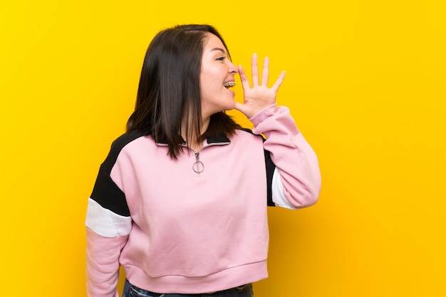 Young Mexican woman over isolated yellow background shouting with mouth wide open