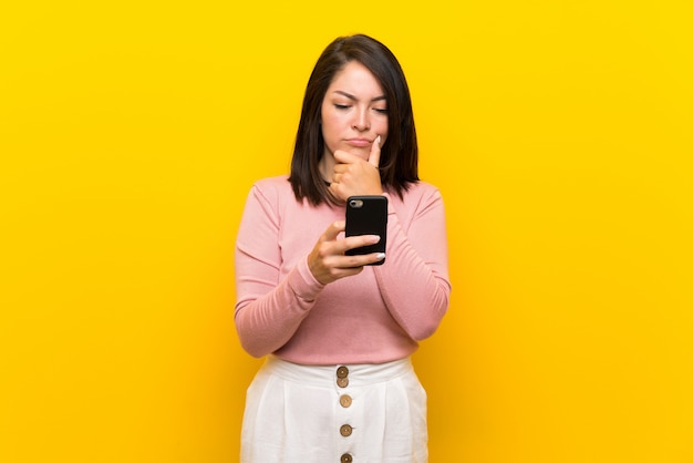 Young Mexican woman over isolated yellow background thinking and sending a message