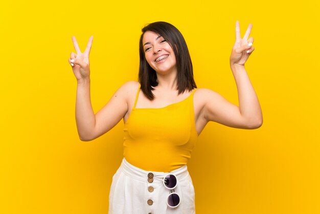 Young Mexican woman over isolated yellow showing victory sign with both hands