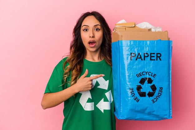 Young mexican woman recycling cardboard isolated on pink background pointing to the side