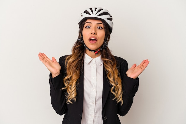 Young mexican woman riding a bicycle to work isolated on white wall surprised and shocked.