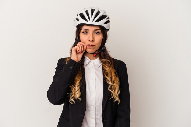 Young mexican woman riding a bicycle to work isolated on white wall with fingers on lips keeping a secret.