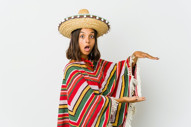 Young mexican woman shocked and amazed holding a copy space between hands.