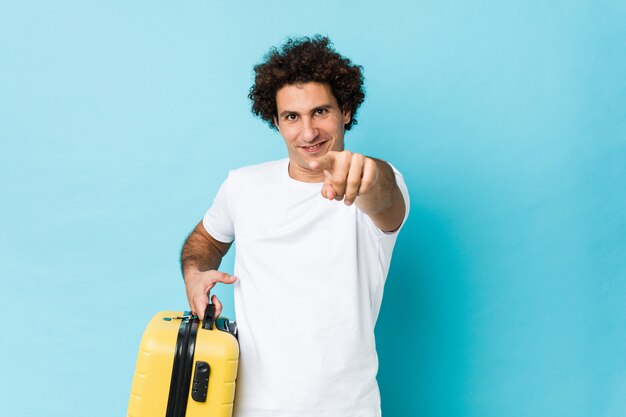 Young middle aged man holding a suitcase cheerful smiles pointing to front