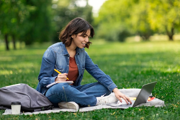 Giovane donna mediorientale studio all'aperto con laptop e blocco note