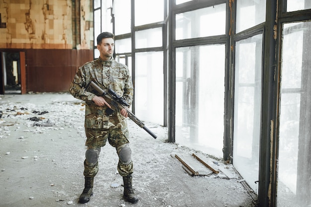 A young military soldier patrols a building with a big rifle