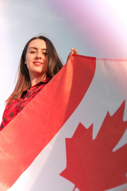 Young millennial brunette woman holding the national flag of canada canadian flag or the maple leaf