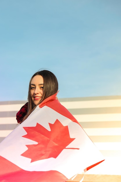 Young millennial brunette woman holding the national flag of canada canadian flag or the maple leaf