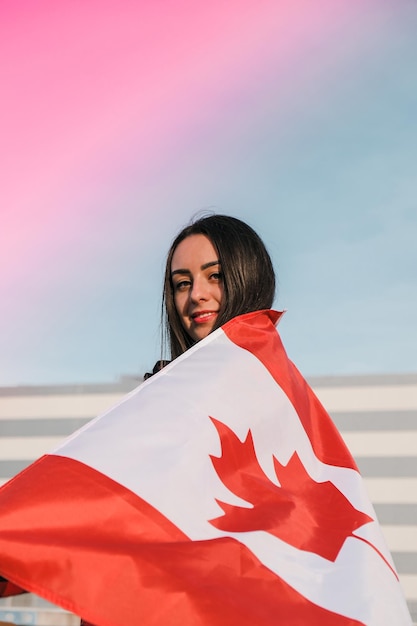 Young millennial brunette woman holding the national flag of canada canadian flag or the maple leaf