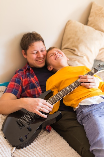 Young millennial man, father and cute son playing electric guitar. Stay at home, home activity, learning classes, family having fun time together