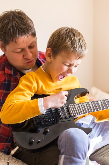 Young millennial man father and cute son playing electric guitar Stay at home home activity learning classes family having fun time together