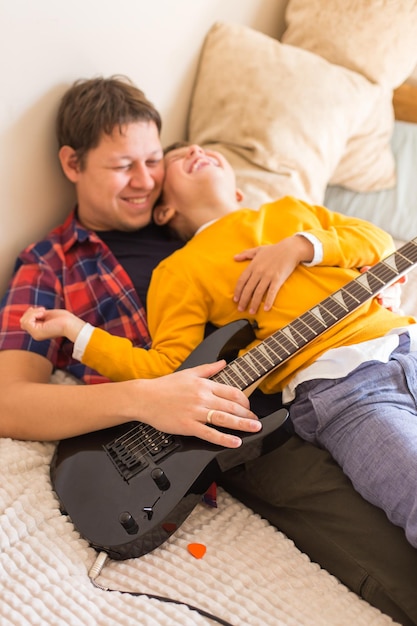 Young millennial man father and cute son playing electric guitar Stay at home home activity learning classes family having fun time together