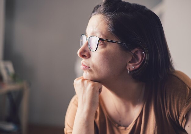 Foto giovane madre millenaria a casa che indossa occhiali da vista guardando in lontananza triste e depressa