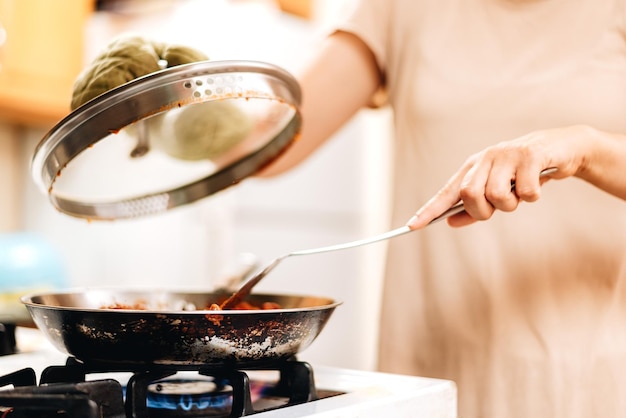 Foto giovane donna millenaria a casa in cucina che cucina sulla stufa a gas o sulla stufa