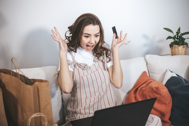 自宅でオンラインショッピングをする若いミレニアル世代の女性。ノートパソコンとクレジットカードを使用して新しいものを購入する女性。